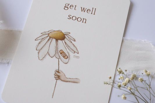 Postkarte mit zarter handgezeichneter Blume und Pflaster, darüber der Spruch „Get Well Soon“ – liebevolle Gute-Besserungskarte auf Naturpapier.