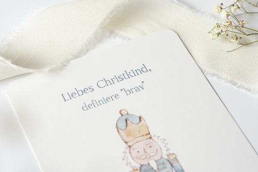 Postkarte „Liebes Christkind, definiere ‚brav‘“ mit liebevoller Illustration eines Nussknackers – humorvolle Weihnachtskarte