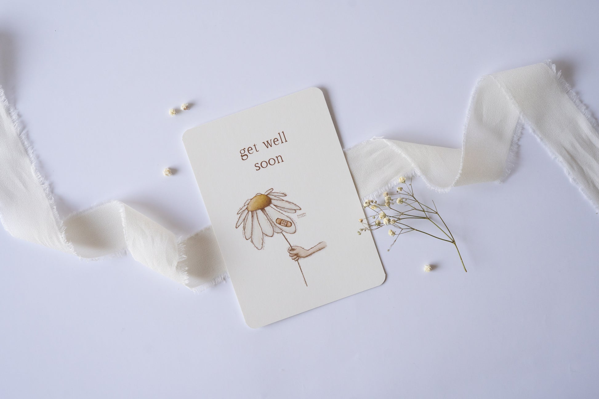 Postkarte mit zarter handgezeichneter Blume und Pflaster, darüber der Spruch „Get Well Soon“ – liebevolle Gute-Besserungskarte auf Naturpapier.