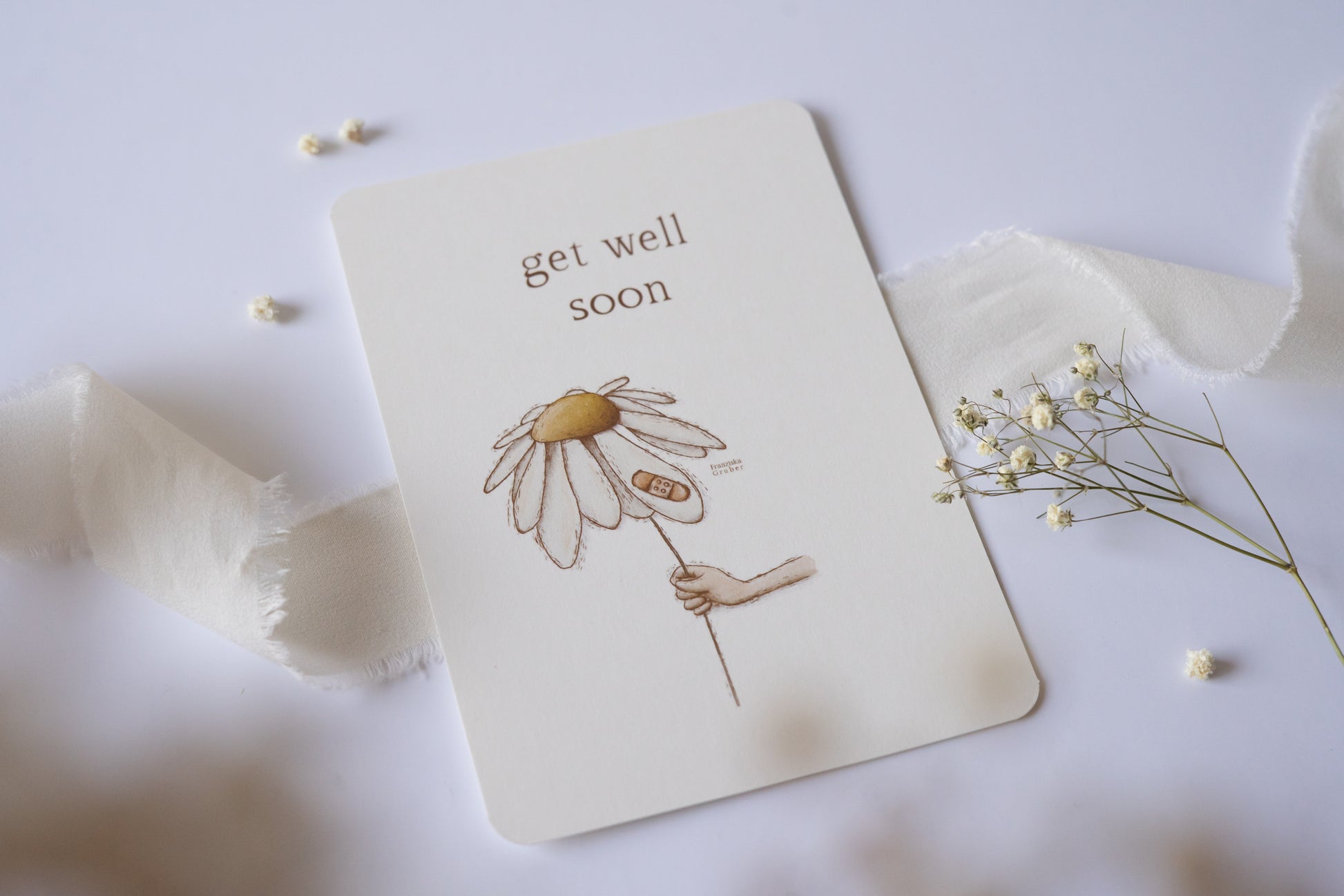 Postkarte mit zarter handgezeichneter Blume und Pflaster, darüber der Spruch „Get Well Soon“ – liebevolle Gute-Besserungskarte auf Naturpapier.