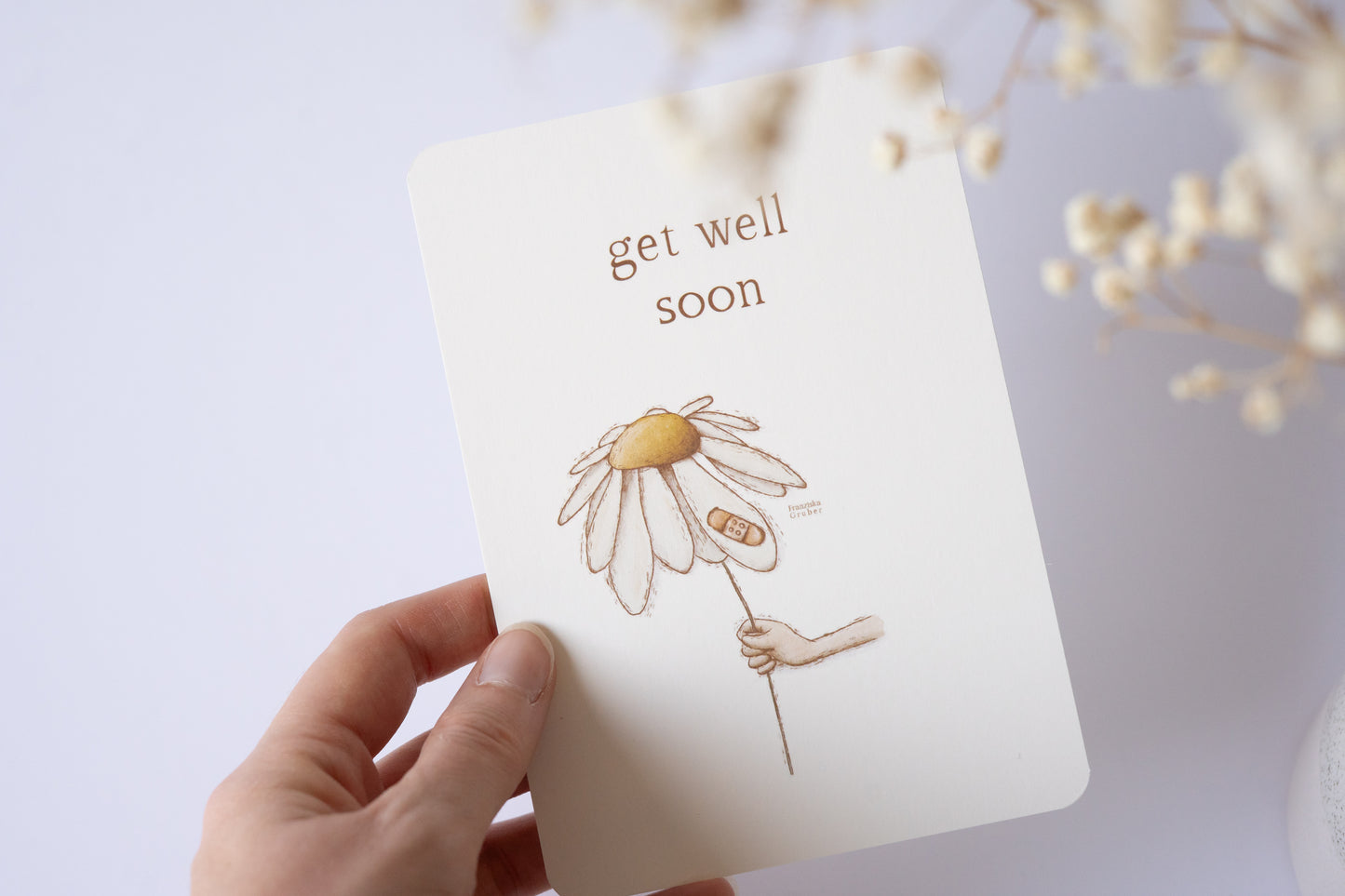Postkarte mit zarter handgezeichneter Blume und Pflaster, darüber der Spruch „Get Well Soon“ – liebevolle Gute-Besserungskarte auf Naturpapier.