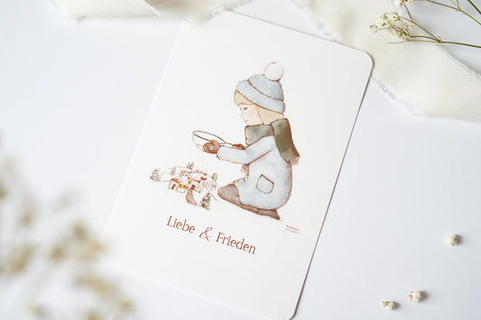 Postkarte mit winterlicher Illustration eines Kindes vor einem Dorf und dem Text „Liebe & Frieden“, Weihnachtskarte A6 von FranziGruDesign