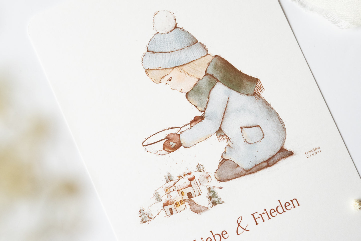 Postkarte mit winterlicher Illustration eines Kindes vor einem Dorf und dem Text „Liebe & Frieden“, Weihnachtskarte A6 von FranziGruDesign