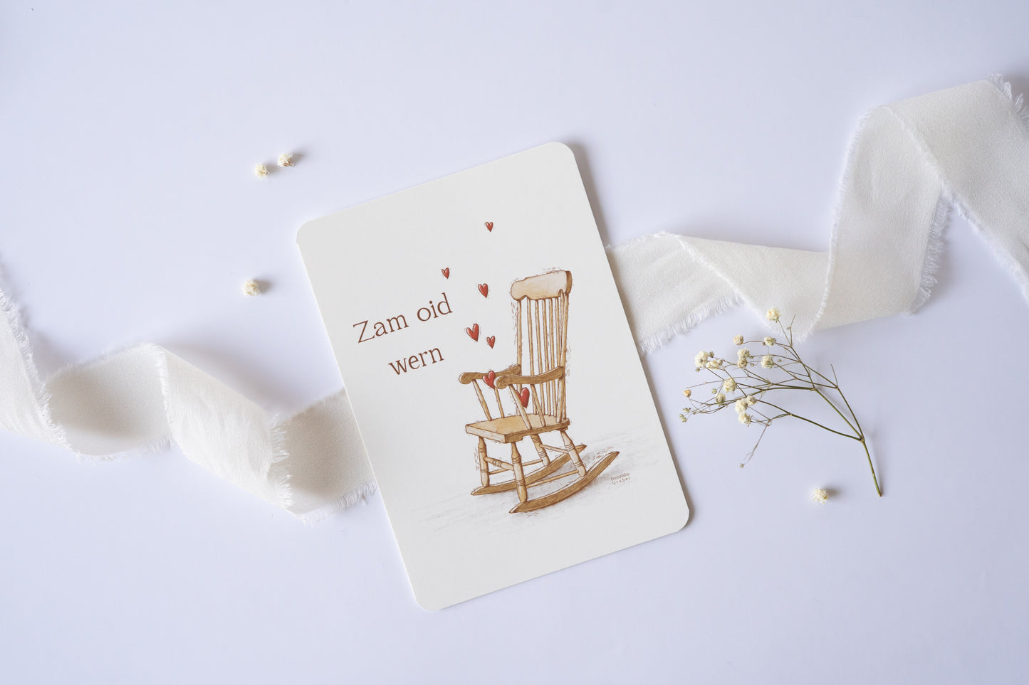 Postkarte „Zam oid wern“ im bayerischen Dialekt mit handgezeichneter Schaukelstuhl-Illustration und roten Herzen – ideal für Hochzeit oder Jahrestag.