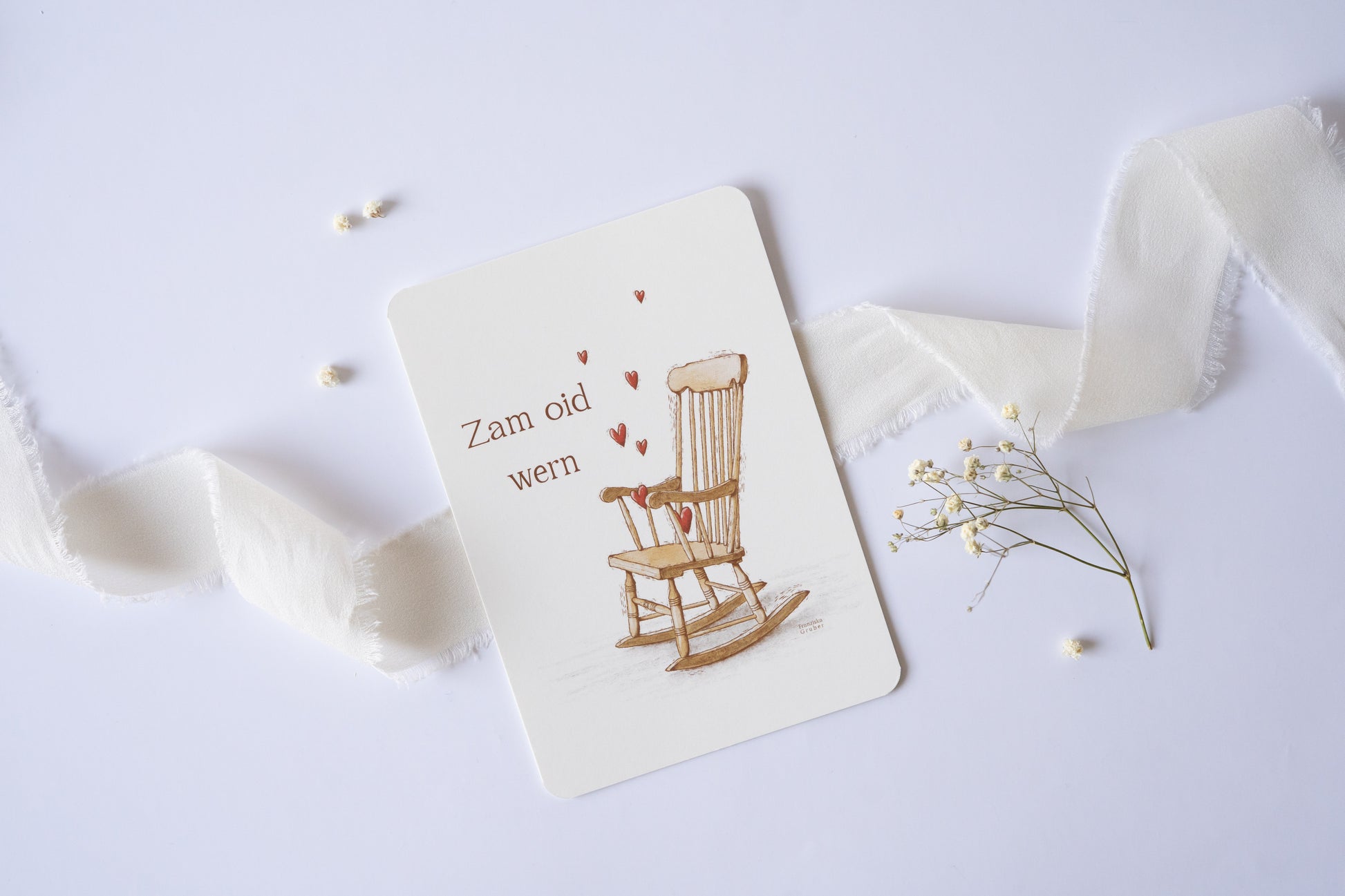 Postkarte „Zam oid wern“ im bayerischen Dialekt mit handgezeichneter Schaukelstuhl-Illustration und roten Herzen – ideal für Hochzeit oder Jahrestag.