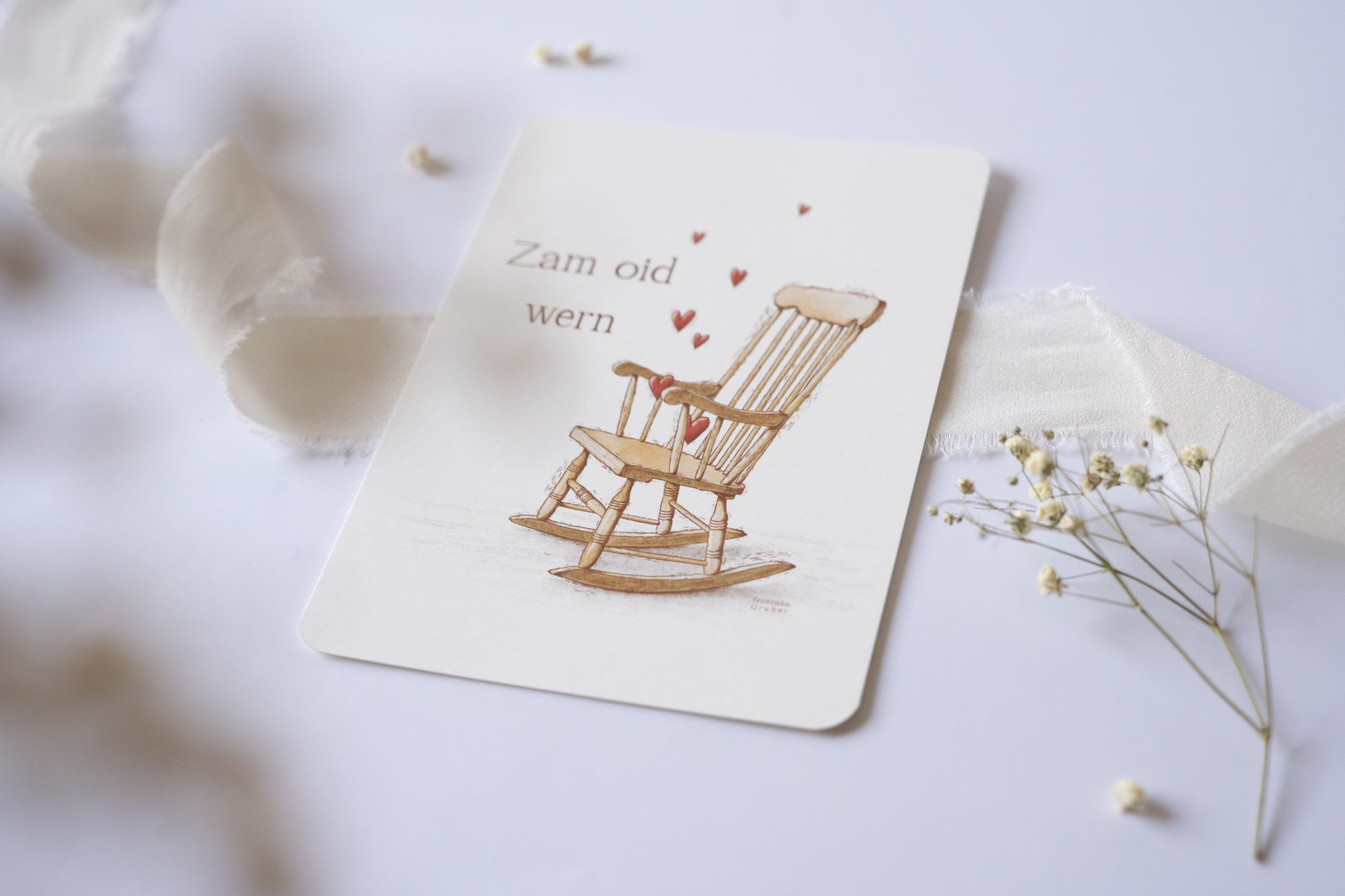 Postkarte „Zam oid wern“ im bayerischen Dialekt mit handgezeichneter Schaukelstuhl-Illustration und roten Herzen – ideal für Hochzeit oder Jahrestag.