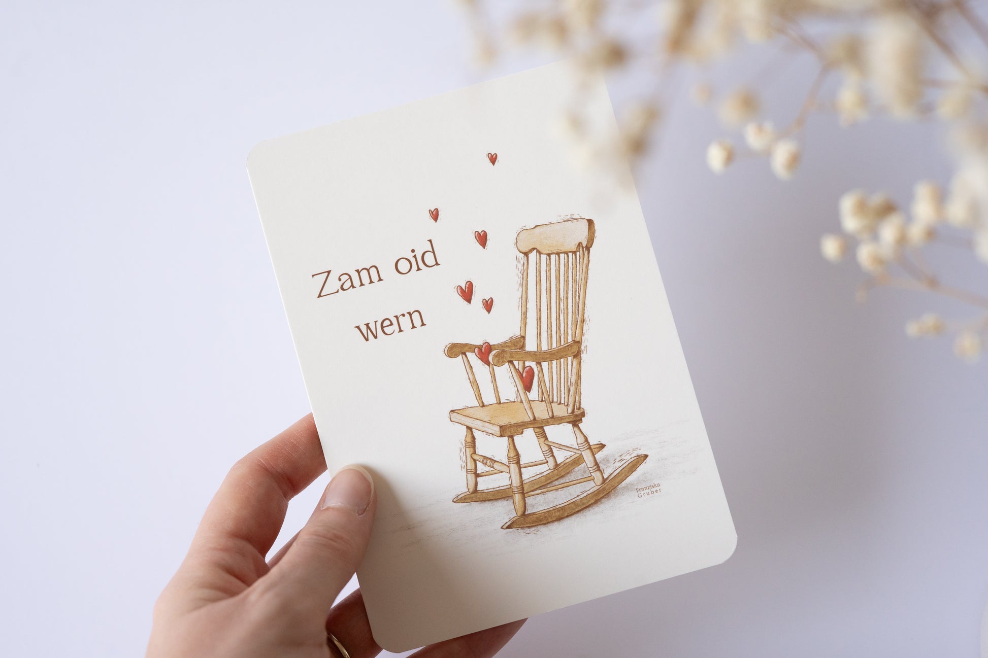 Postkarte „Zam oid wern“ im bayerischen Dialekt mit handgezeichneter Schaukelstuhl-Illustration und roten Herzen – ideal für Hochzeit oder Jahrestag.