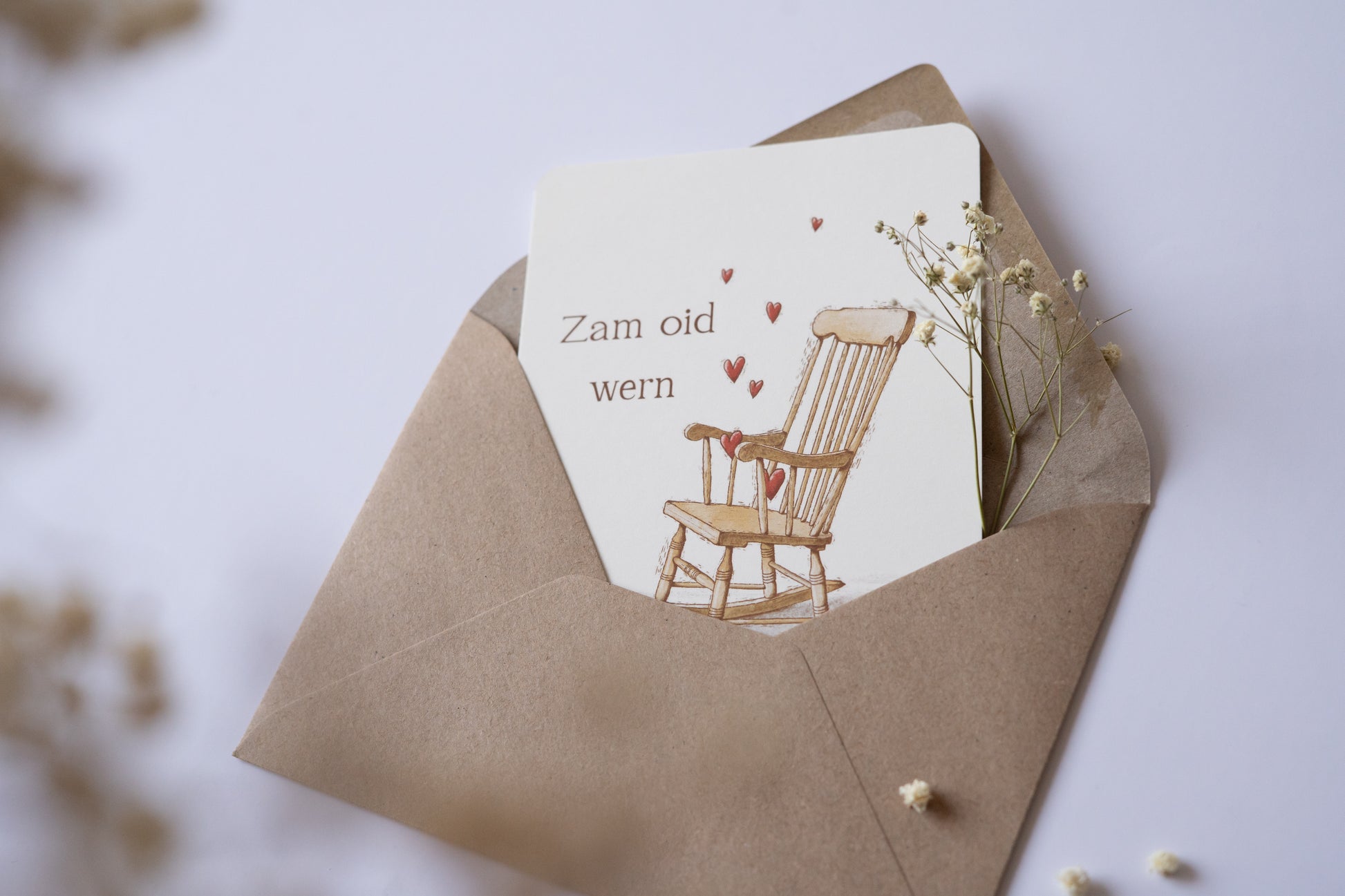 Postkarte „Zam oid wern“ im bayerischen Dialekt mit handgezeichneter Schaukelstuhl-Illustration und roten Herzen – ideal für Hochzeit oder Jahrestag.